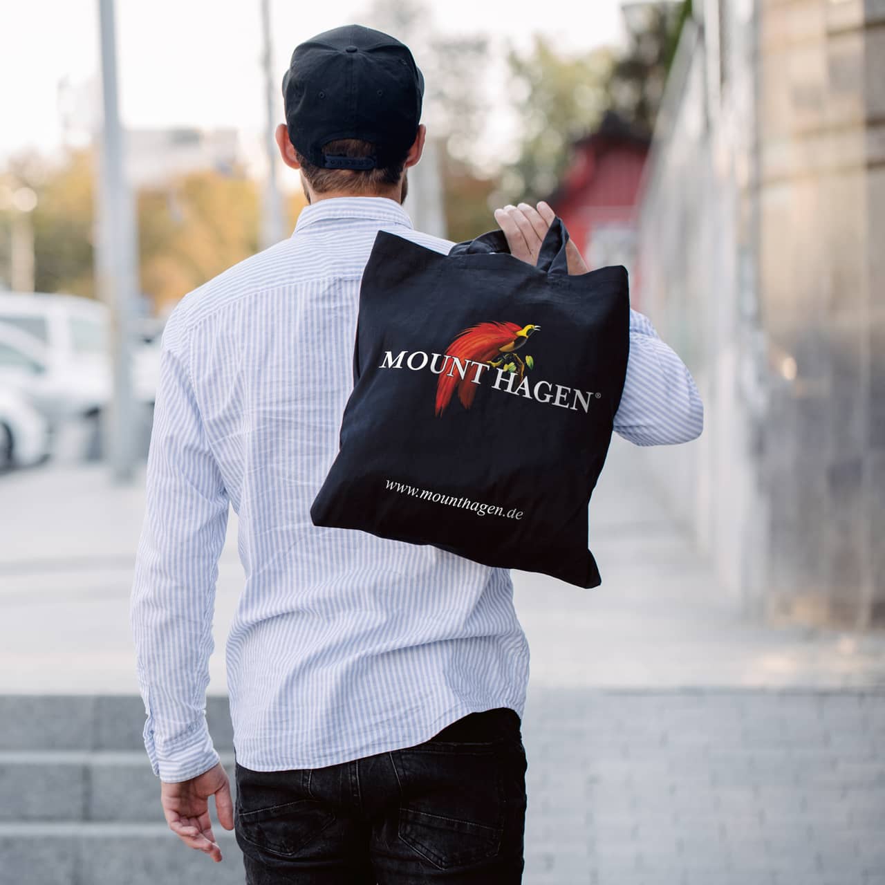 Young man holding black textile eco bag against urban city background. . Ecology or environment protection concept. Black eco bag for mock up